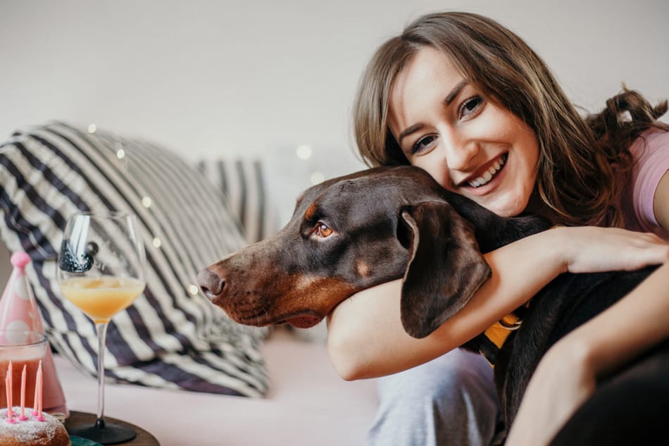 Girl tightly hugs her Doberman Pinscher.