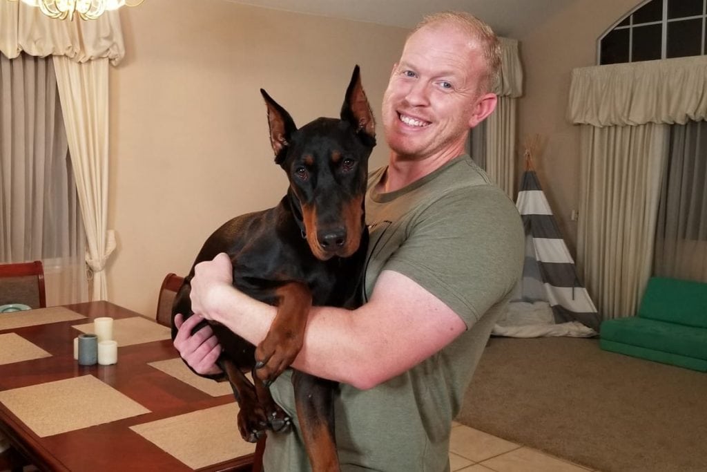 Man holding his Doberman close to his chest off the ground. Hugging.