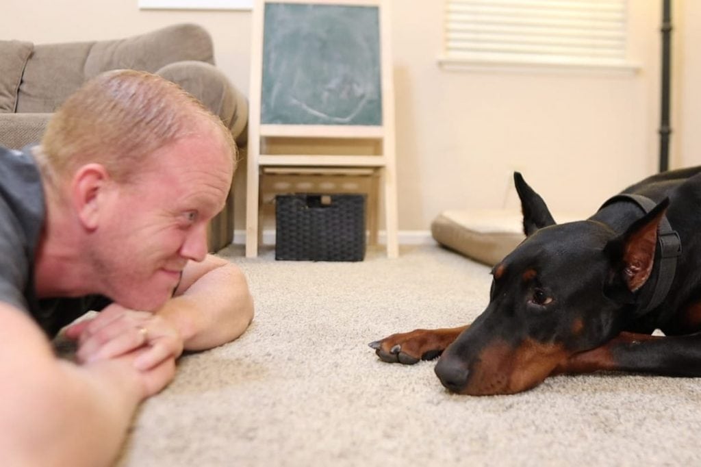Man laying on the ground looking face to face with his Doberman up close.